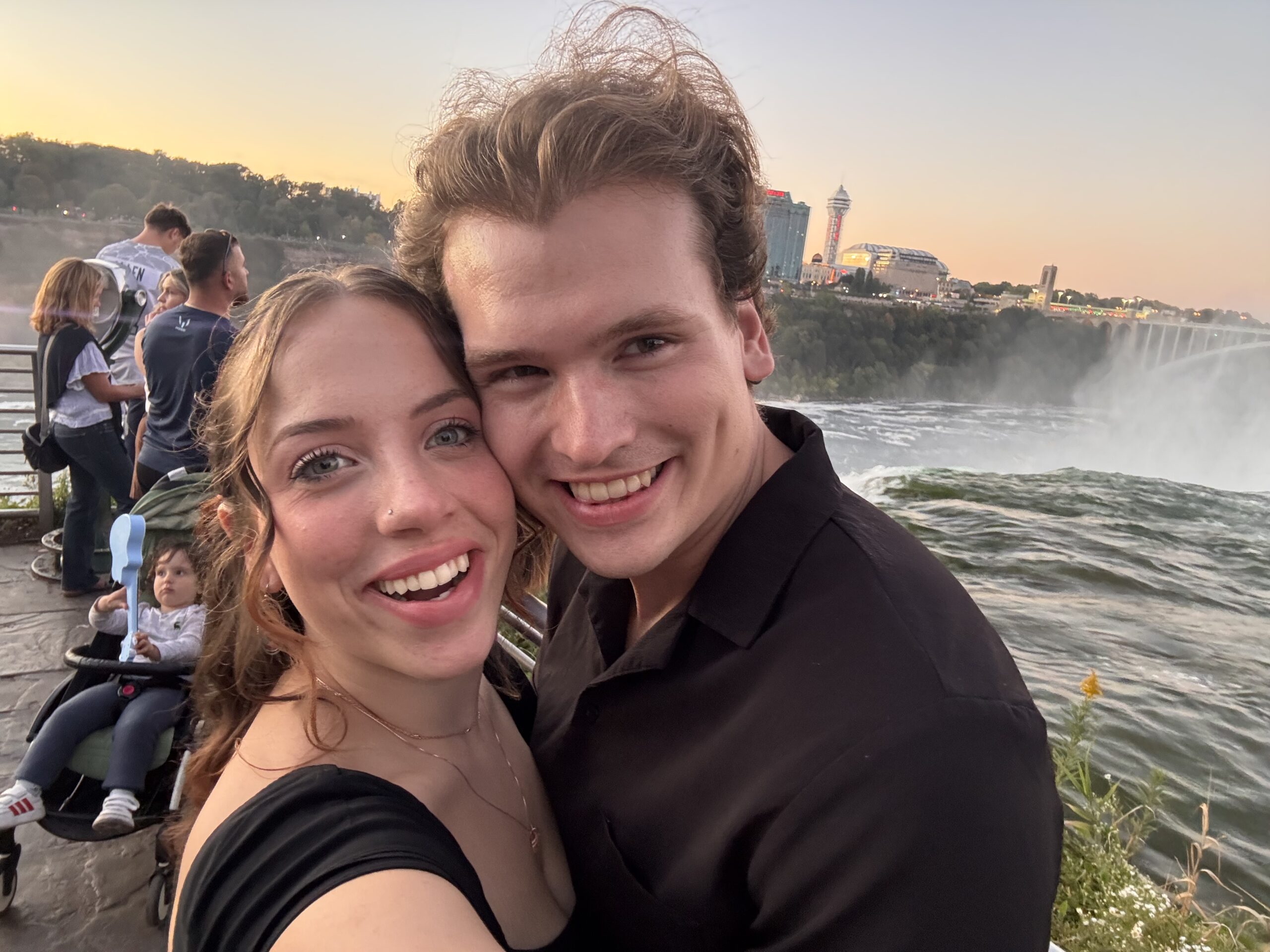 Stephen and Cianna Holmes smiling together beside a waterfall at sunset.