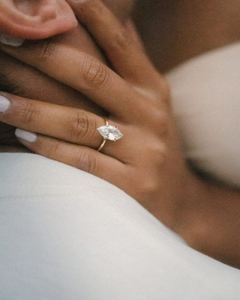 Close-up of an engagement ring as a couple embraces.