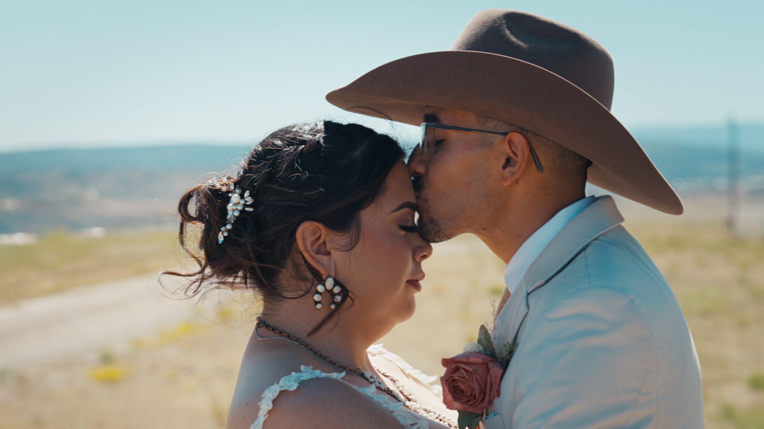Groom in a cowboy hat kissing the bride’s forehead.