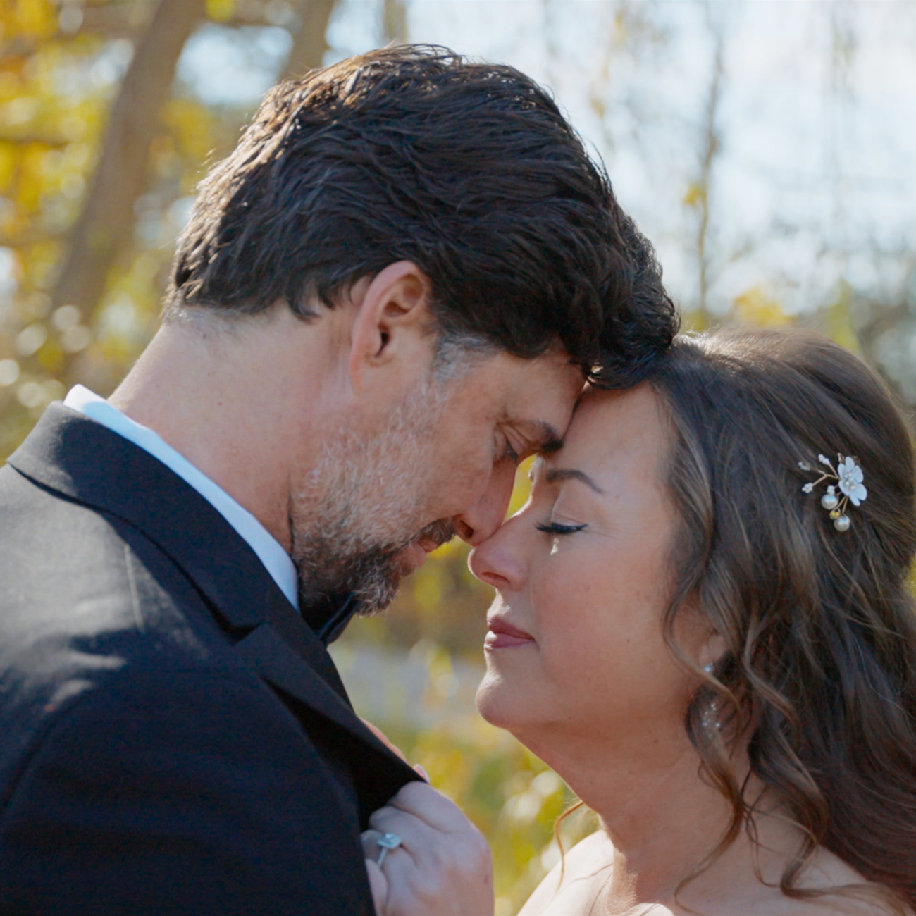 Bride and groom touching foreheads beneath autumn trees.
