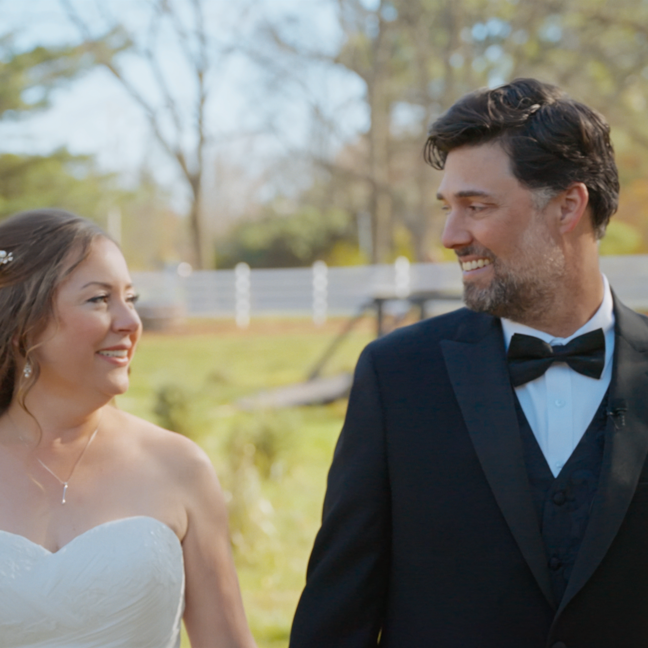 Bride and groom smiling at each other outdoors.