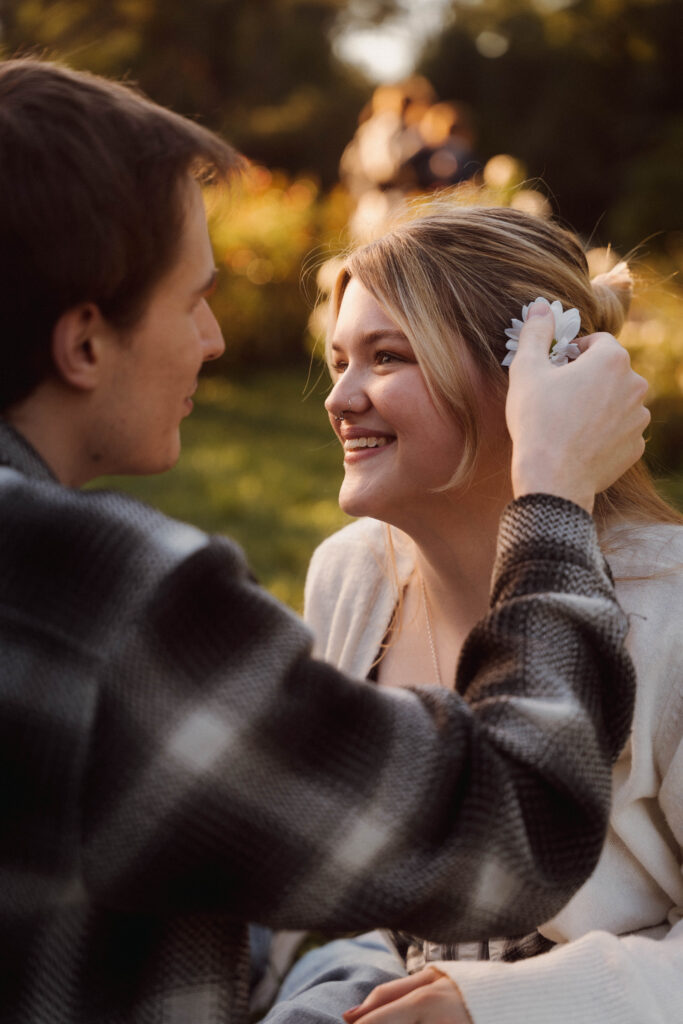 Man tucking a white flower into his smiling partner’s hair.