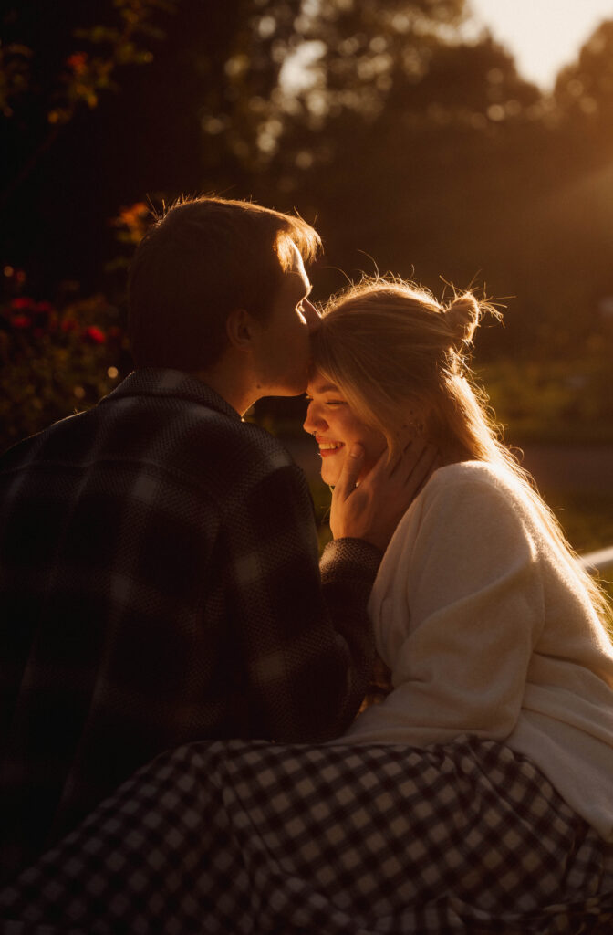 Man kissing his partner’s forehead as they sit together in golden evening light.