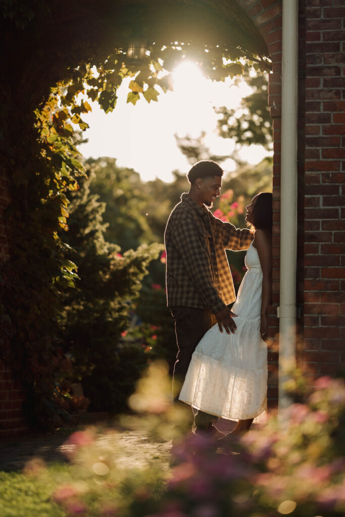 Couple sharing a quiet moment beside a brick column in warm evening sunlight.