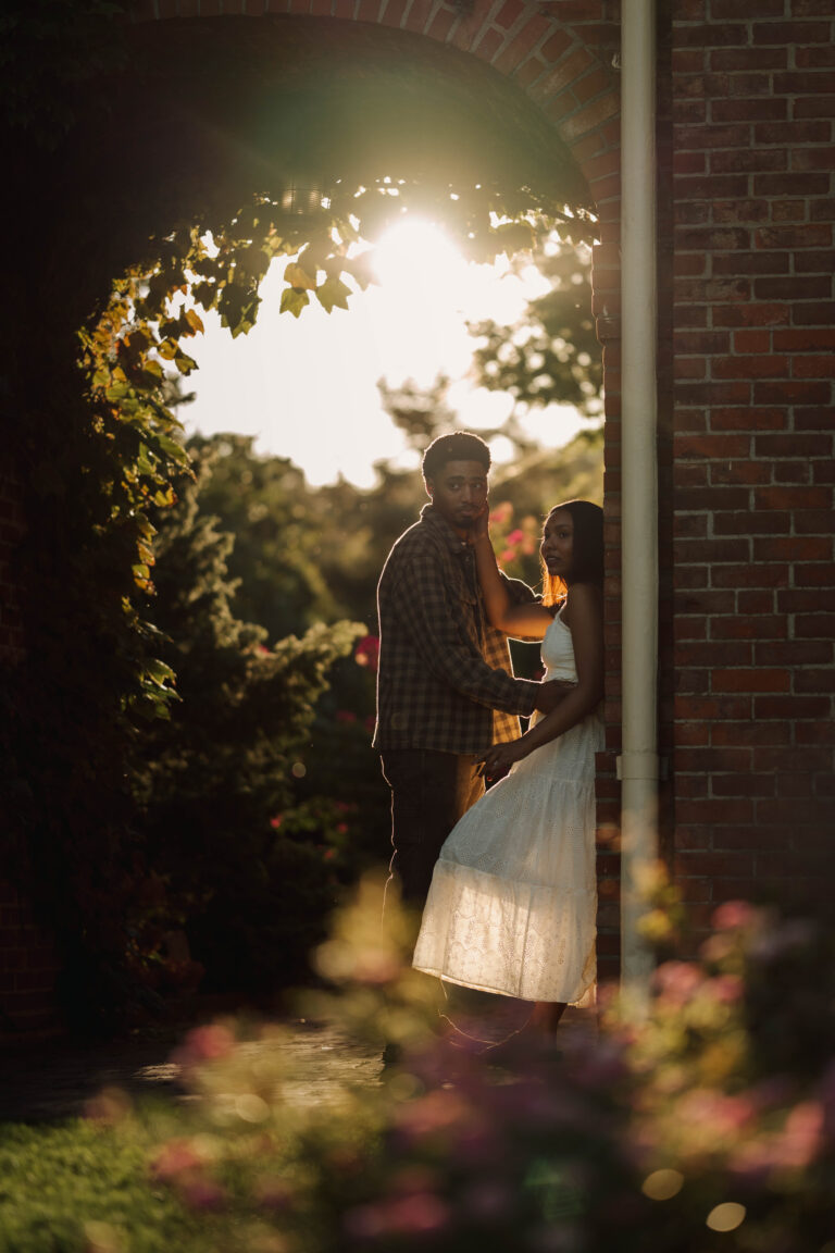 Couple sharing a quiet moment beside a brick column in warm evening sunlight.