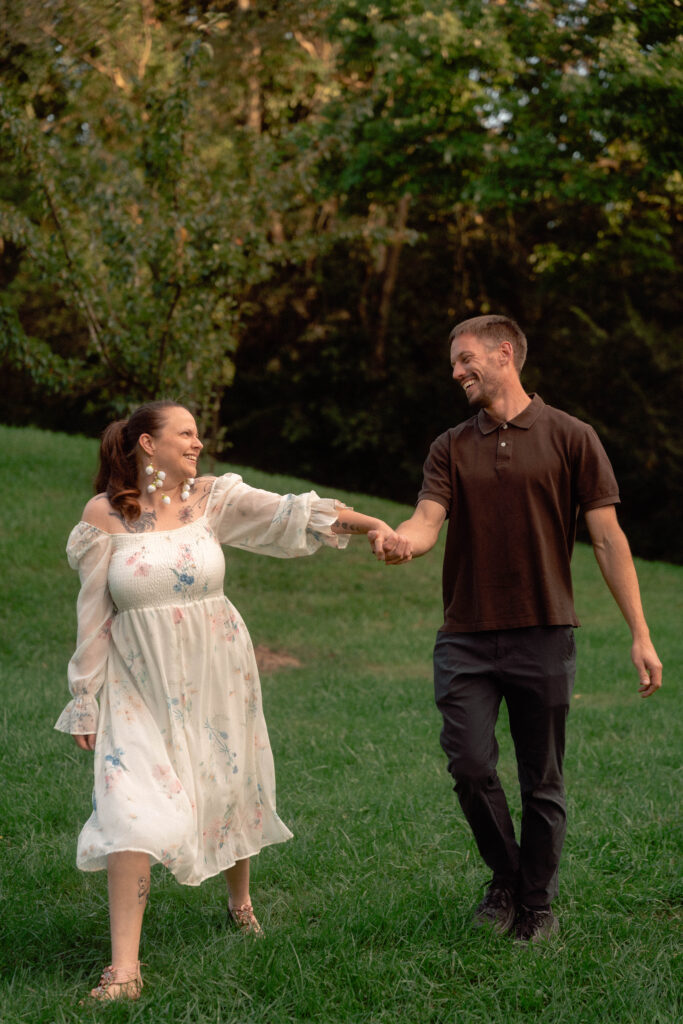 Couple smiling and holding hands as they twirl on a grassy lawn.