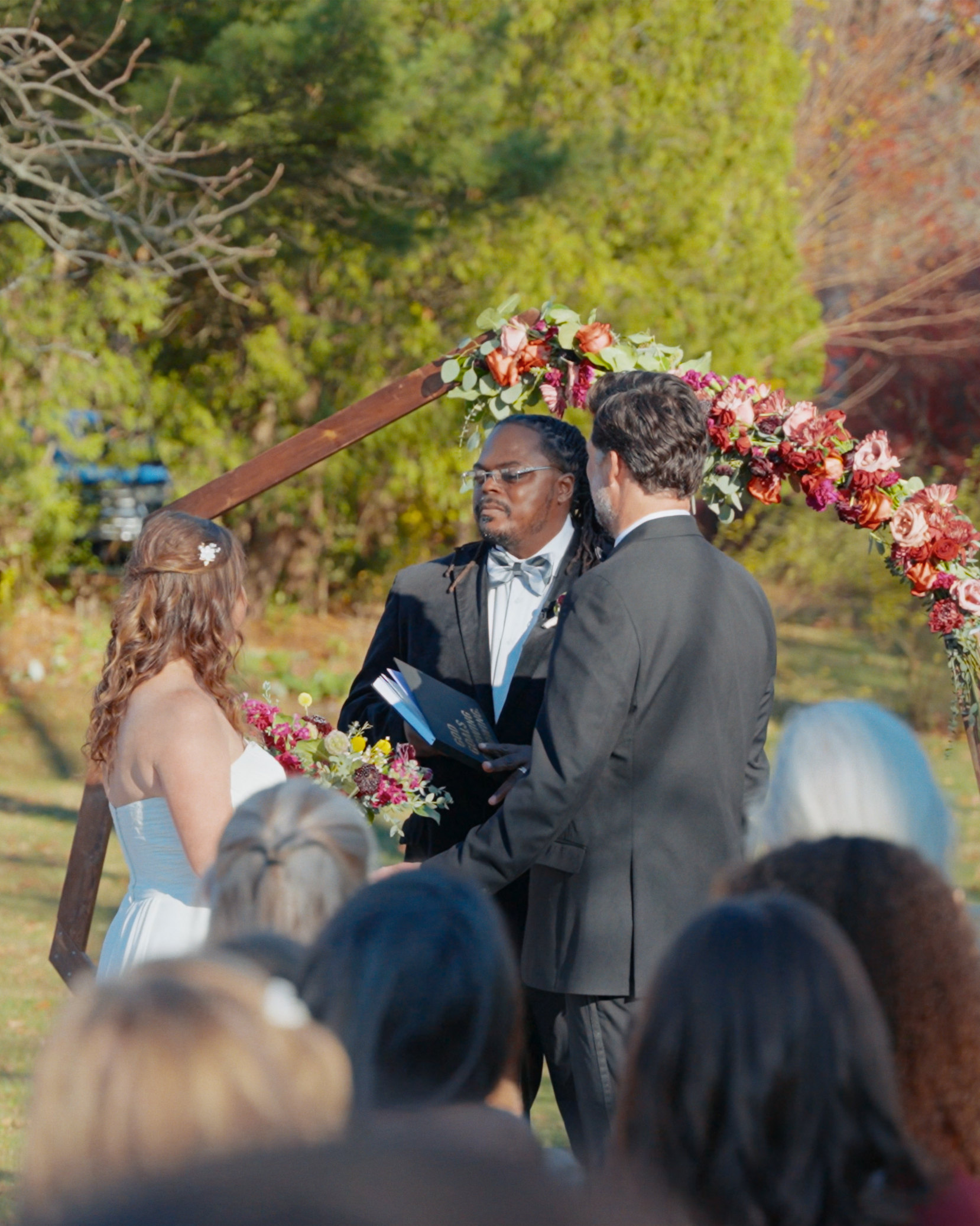 Bride and groom during an outdoor wedding ceremony beneath a floral arch.