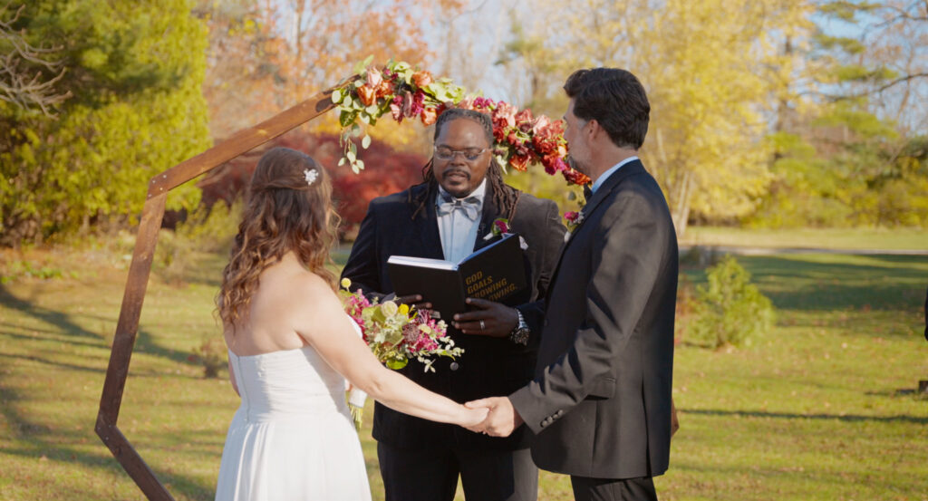 Couple exchanging vows beneath an arch surrounded by autumn foliage.