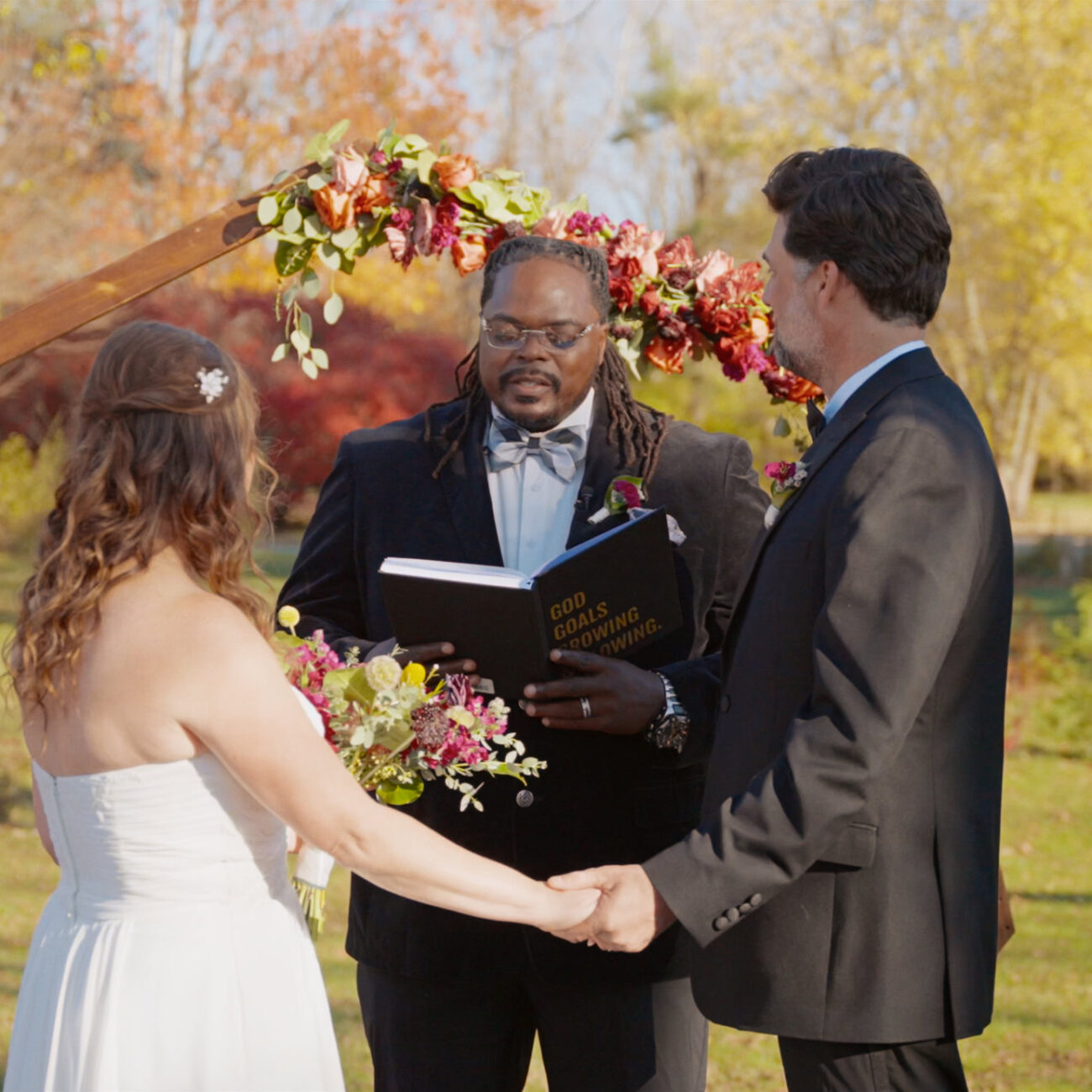 Couple exchanging vows beneath an arch surrounded by autumn foliage.